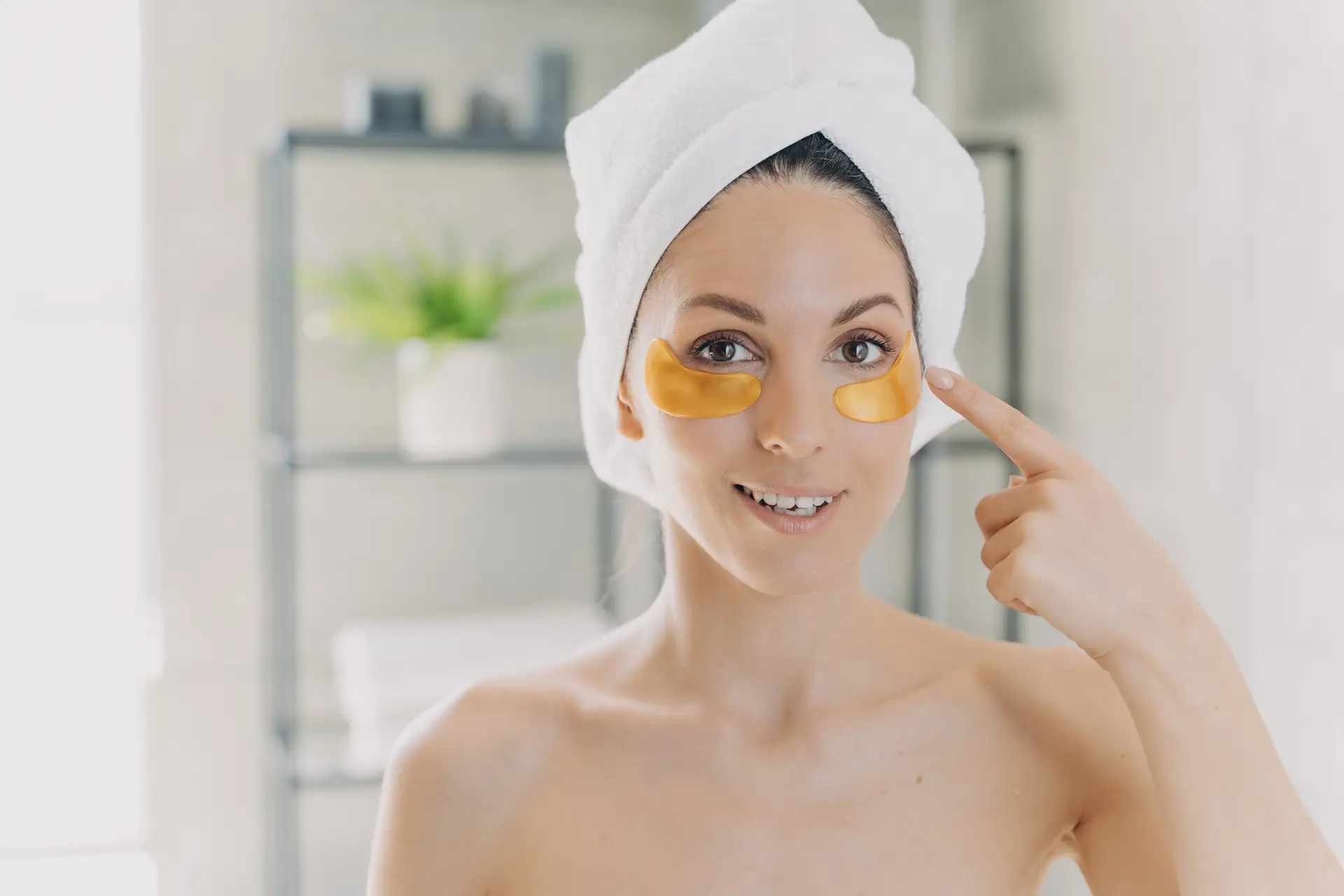 Female shows under eye collagen golden patches standing in bathroom. Skincare, eye skin treatment
