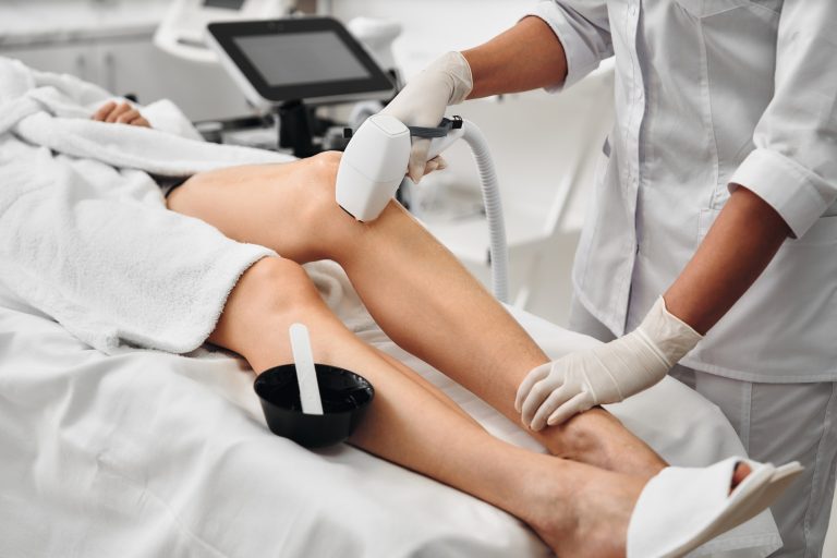 Aesthetician performing laser hair removal on a clients leg in a clinic