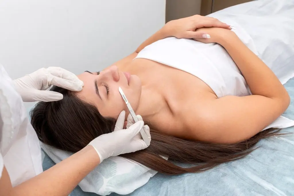 Closeup of the doctor with a scalpel treating the woman's skin. Dermaplaning treatment.
