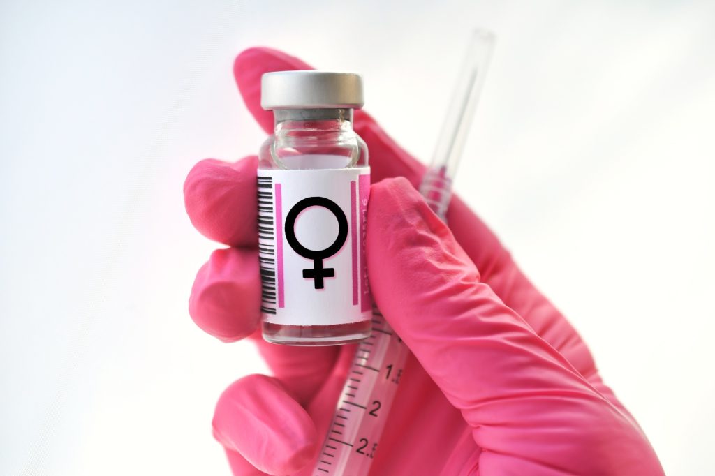 Pink gloved hand holding a vial with female symbol, hormones injections, concept hormone replacement